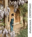 Small photo of a woman in denim dress and embroidered jacket by blooming flowers near Marie Antoinette's little house