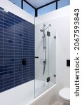Small photo of Shower with blue wall tiles, faucet and black shower head, toilet, white bath and elongated window on black frame