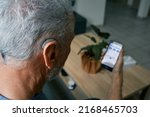 Small photo of Hearing impaired senior man adjusting settings for his BTE hearing aid via smartphone. Hearing aids with innovative technologies at audiology