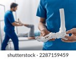 Small photo of Podiatrist showing anatomical foot skeleton model during his assistant examination injured leg of patient in department of traumatology and orthopedics