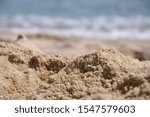 Small photo of A close-up of a sand heap - shot so close that it looks like a mountain hill. In the back - blurry image of the white waves of the Black sea. An abstract closeup view of the prosaic. A macro beach.