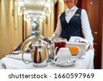 Waitress in uniform delivering tray with food in a room of hotel. Room service. Selective focus on tableware. Horizontal shot