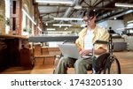 Small photo of Portrait of young male office worker in a wheelchair looking at the screen of his laptop while performing in co-working space. Disability and handicap concept. Horizontal shot. Selective focus