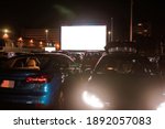 Small photo of The best place to go. Many cars parked in front of a big white screen to watch movies or films sitting inside the car at drive in cinema in the evening. Entertainment, hobby concept