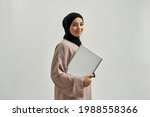 Happy young arabian girl holding laptop while posing on light background and smiling at camera. Beautiful muslim lady