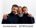 Portrait headshot of three generations of men hug cuddle show family love and unity together. Caring old grandfather embrace protect young adult grownup son and little grandson. Descendant.