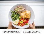 Small photo of Hands holding salmon and buckwheat dish with green beans, broad beans, and tomato slices. Nutritious dish with vegetables and fish from above. Healthy balanced diet