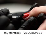 Small photo of Manicurist makes a hardware manicure to a client of a beauty salon. The master applies a decorative bright red varnish on the nail plate with a brush. The concept of beauty and nail care.