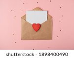 Craft envelope with a blank sheet of paper inside and red wooden heart on the rose background. Romantic love letter for the Valentine's day concept. Space for text.