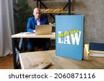 Small photo of Jurist holds MARTIAL LAW book. Martial law is the temporary imposition of direct military control of normal civil functions or suspension of civil law by a government