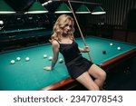 Blond woman playing enjoying billiard, hold cue, white billiard balls on table with green surface in billiard club. Pool game snooker pyramid player
