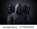 Group of three scary figures in hooded cloaks in the dark