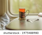A glass cup with tea in an iron cup holder is on the table in the train carriage by the window. Travel hot drink. Travel concept.
