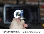 Small photo of A blue halogen light bulb in the man's hand. A professional worker changes the new halogen lamps of the car. Car repair. The mechanic holds a blue halogen lamp in his hand in close-up.