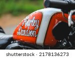 Small photo of St. Petersburg, RUSSIA - On June 14, 2022, a modified Harley-Davidson motorcycle on a clear summer day. The gas tank of a red Harley Davidson on a clear sunny day in drops after rain.