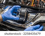 Car headlight in repair close-up. An auto mechanic wearing gloves installs the lens into the headlight housing. Installation of Bi-LED lenses in the headlight. Bi-LED lenses.