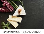 Small photo of Delicious brie cheese on black background. Brie type of cheese. Camembert. Fresh Brie cheese and a slice on stone board. Italian, French cheese.