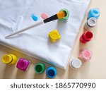 Fabric painting on fabric. White cotton fabric, fabric watercolors colors, brush - painting accessoires on wooden background.  DIY creative project, hobby, sewing, and tailor tools.