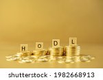 HODL written on wooden blocks on stack of bitcoins on golden background. Acronym standing for 'hold on for dear life' in cryptocurrency concept.
