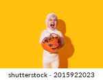 Child in mummy costume holding basket of chocolates in front of yellow background.
