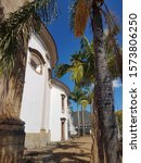 Small photo of Mariana, Minas Gerais, Brazil - September 5, 2018: The white rounded side facade of the Saint Peter of the Clergymen Church in Mariana on a sunny day. A historical baroque building with palm trees.