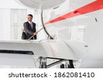 Businessman with the suitcase looking back while standing on the steps of a private jet