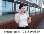 Small photo of Adorable brunette woman with happy look having sunglasses on head and wearing white blouse siting over modern cafe interior, using cell phone, checking newsfeed on her social network accounts.