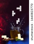 Small photo of Splash. Plop. Tea and falling sugar cubes in tetris shapes.Cup of tea against blue background, cardamom, whole cinnamon, mint and sugar cubes in unusual shapes.
