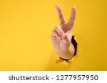 Hand showing peace gesture through torn yellow paper background. Victory, V sign.