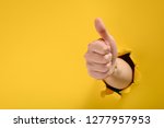 Hand showing a thumb up sign through a ripped hole in yellow paper wall. Well done, good job concept.