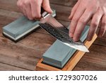 Man sharpens a Gyuto knife using a whetstone on a rustic wooden table. Japanese knife with Damascus steel.