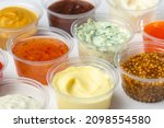 Variety of different sauces and condiments in small cups on white table. Mayonnaise, cheese sauce, pesto, mustard, sweet and sour sauces.