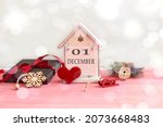 Calendar for December 1: decorative house with the name of the month in English, number 01, gift wrapped, tied with a red ribbon, red heart, New Year's toys, bokeh.
