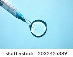 Transparent drop of hyaluronic acid gel and a medical syringe for injections on a blue background. Top view, place for text.