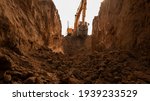 The excavator digs a trench for laying the pipeline. View from the trench. Clay soil. Part of the image is blurred.