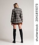 Small photo of girl in high autumn boots and a plaid fagot posing from the back