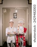 Small photo of Surabaya, Indonesia - 22 february 2024: a couple taking photos holding a marriage certificate and dowry while wearing traditional white Javanese clothes