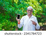 Small photo of Indian farmer shoving smartphone in farm field.