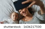 Small photo of Authentic close up of neo mother and her newborn baby making a selfie or video call to father or relatives in a bed. Concept of technology, new generation,family, connection, parenthood, authenticity