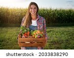 Authentic shot of happy farmer holding basket with fresh harvested at the moment vegetables and smiling in camera on countryside field. Concept:biological, bio products, bio ecology, vegetarian, vegan