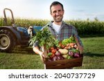 Authentic shot of happy farmer holding basket with fresh harvested at the moment vegetables and smiling in camera on countryside field. Concept:biological, bio products, bio ecology, vegetarian and vegan