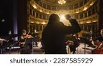 Small photo of Back View of Professional Conductor Directing Symphony Orchestra with Performers Wearing Medical Masks, Playing Violins, Cello and Trumpet on Classic Theatre with Curtain Stage During Music Concert