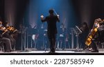 Small photo of Cinematic Shot of an Orchestra on a Classic Theatre Stage: Professional Conductor Directing Symphony Orchestra with Performers Playing Violins, Cellos, and Trumpets During Music Concert