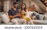 Small photo of Young Indian Couple Sitting On The Sofa at Home: Woman Annoyed at her Boyfriend for Spending Too Much Time Online on Smartphone. She Takes Away his Phone. Social Media and Doom Scrolling Addiction