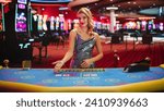 Small photo of Portrait of a Female Croupier Looking at the Camera and Sharing the Results of a Baccarat Card Game. Beautiful Dealer in the Live Online Video Casino Revealing a Winning Hand