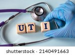 Small photo of A hand in a medical glove puts cubes with the abbreviation UTI (Urinary Tract Infection) on the background of a stethoscope. Medical concept