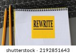 Small photo of REWRITE - word on a yellow piece of paper on the background of a laptop with a notebook and a pen. Business concept
