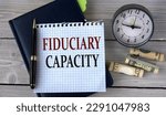 Small photo of FIDUCIARY CAPACITY - words in a white notebook on the background of an alarm clock and a banknote. Business concept