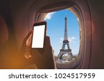 Woman sitting by aircraft window and using a digital mobile during the flight. Eiffel tower as seen through window of an aircraft.