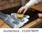 A young woman is cleaning an induction electric hob. Cleaning in the kitchen. Electric oven cleaning. Cleaning company concept.